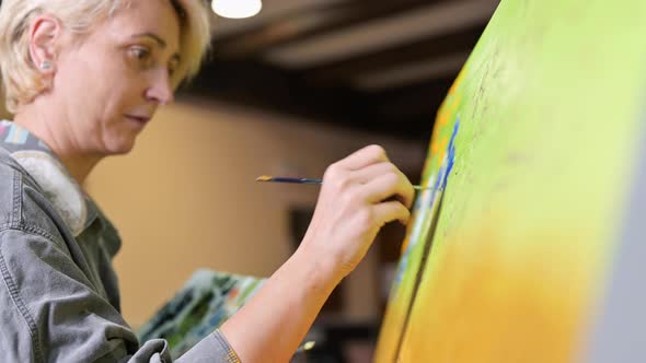 Happy Woman Paints on Canvas Using Thin Brush alt