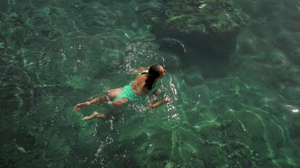 Slow Motion Top View of Sexy Stunning Woman with Nise Buttocks in Green Swimsuit Floating in Clear alt