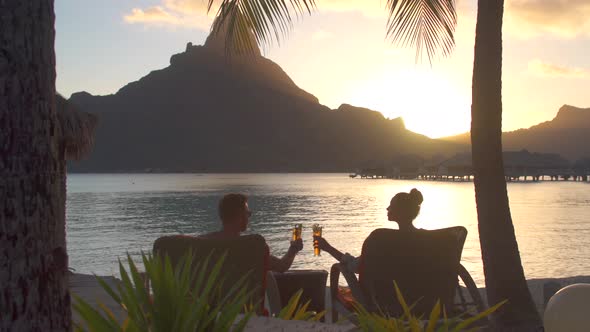 Man and woman couple toasting, drinking drinks, tropical island resort, lagoon and Mount Otemanu alt