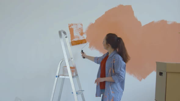 Singleton Lifestyle Concept. Young Happy Woman Paints Her Walls Orange with a Roller alt