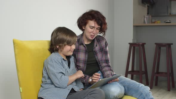 Happy Young Mother and Son Smiling Having Fun Using Digital Tablet Sitting on Sofa