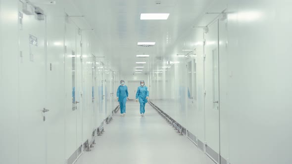 Two Medical Workers in Protective Uniform are Walking in the Hallway of Pharmaceutical Plant