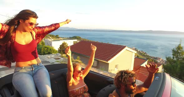 Beautiful young brunette sitting on hood of convertible and dancing to music alt