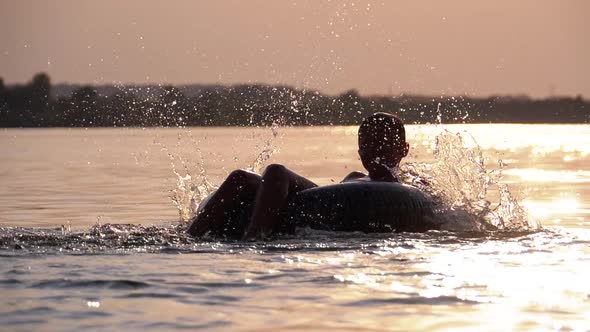 Silhouette of Happy Boy Swiming on Inflatable Circle in the River at Sunset. Slow Motion alt