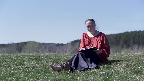 Middle aged female sitting on the grass in the park and enjoying drawing alt
