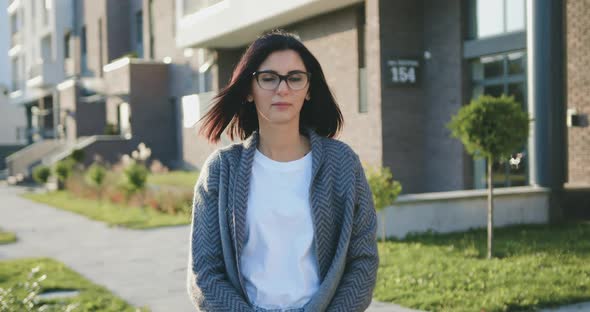 Caucasian Young Woman Looking Into Camera During Walking at Urban Street at Sunset alt