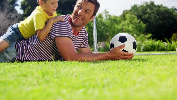 Portrait of happy father and son with football lying in park alt