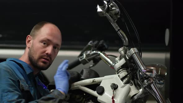 guy mechanic in blue overalls next to a motorcycle