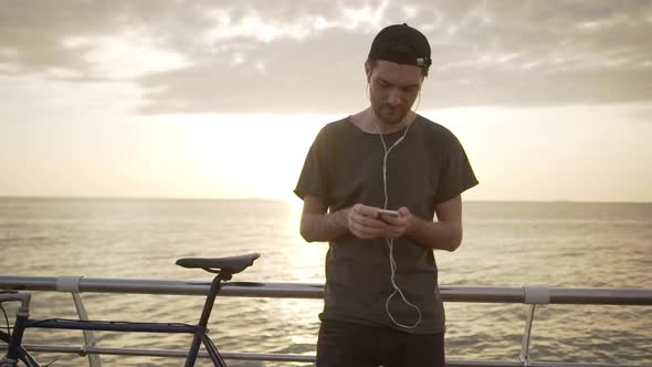 Amazing Sunrise Over Sea with Handsome Man Standing with Bicycle on Seafront Leaning to Metal alt