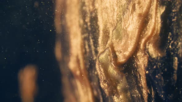 Golden Ink Particles Flows in Water As Colorful Chaos on the Black Background alt