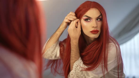 Confident Genderfluid Caucasian LGBT Woman in Red Wig Admiring Reflection in Mirror alt