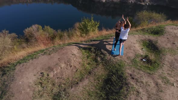 Orbiting Aerial Shot of Family of Three Mother Father and Daughter Do Yoga Exercises on Top of Hill alt