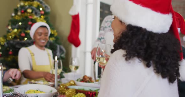 Happy mixed race woman in santa hat celebrating meal with friends at christmas time alt