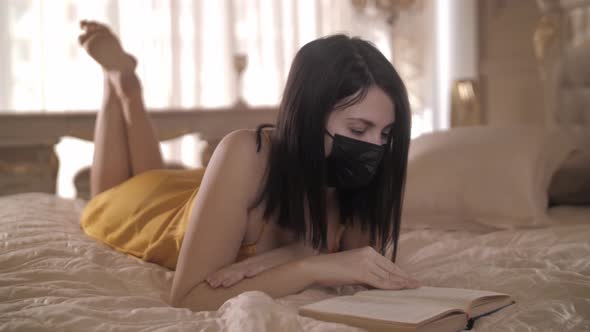 Beautiful Woman in Mask Lying on the Bed and Reading a Book