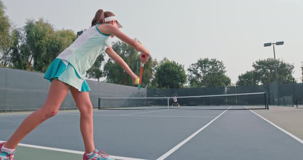 Girl in a Turquoise Dress Hits the Ground with the Ball Before Making a Serve alt