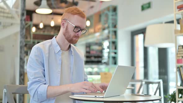 Professional Redhead Man Using Laptop in Cafe alt