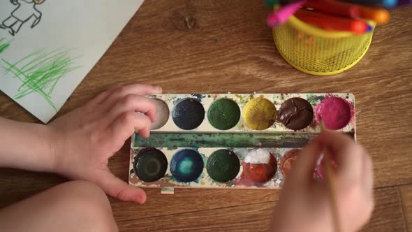A Child on the Floor Draws a Drawing with Watercolors alt