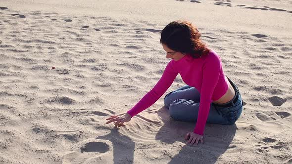 Young Woman Draws a Heart on the Sand