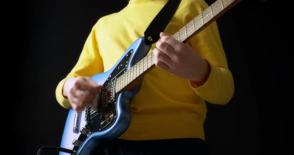 Male Guitarist in a Yellow Jumper Plays an Electric Guitar on Black Background alt