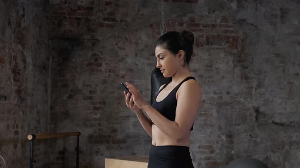 Side view a Young Athletic Indian Woman in Black Leggings and a Top Uses a Smartphone Watches