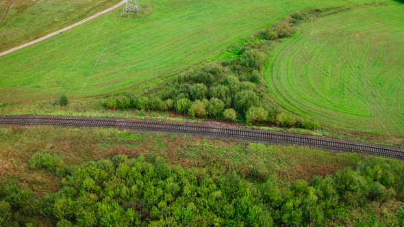 Flying Over Electrical Pylons with Wires Lines on Green Field Near Railway