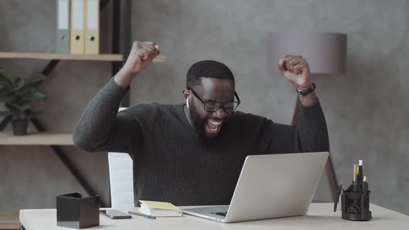 Overjoyed Black Male Student Sit at Desk Look at Laptop Screen Scream Passing Exam Getting High alt