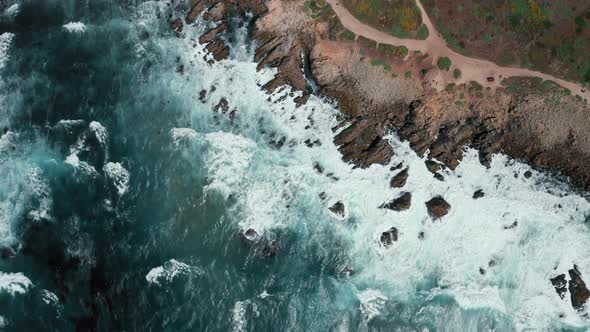 Cinematic Overhead View on the Rocky Shore and Deep Green Clear Ocean Waters alt