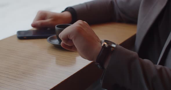 Man Sitting In A Cafe With A Cup Of Coffee Looking At His Watch