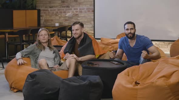 Wide Shot of Cheerful Multiethnic German Football Fans Sitting on Bean Bag Chairs and Cheering Win alt