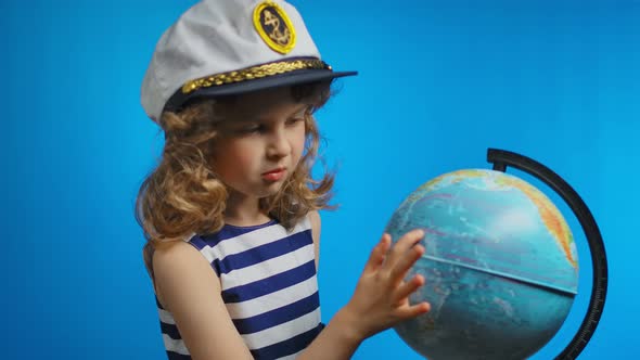 Little Curly Girl in Sailor Hat is Pointing Her Finger Into the Globe alt