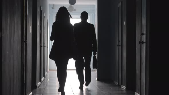 Full Length Silhouettes of Male and Female Colleagues Going through Hallway 