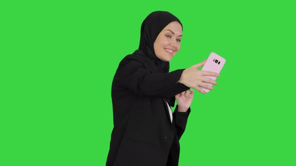 Smiling Arab Woman in Hijab Taking Selfie Pictures on Her Mobile Phone on a Green Screen, Chroma Key alt