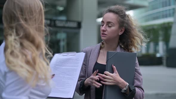 Young woman discussing plans and documents with colleague near office building alt