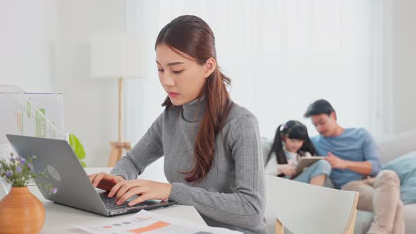 Asian businesswoman mother sit on table in living room, work from home. alt