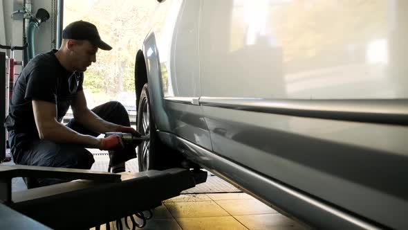 Car mechanic screwing or unscrewing car wheel of lifted automobile at repair service station