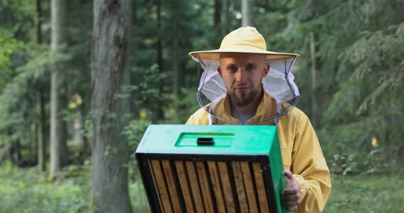 A Young Experienced Smiling Man Engaged in Beekeeping Holds an Apiary of Bees in His Hands Looks at alt