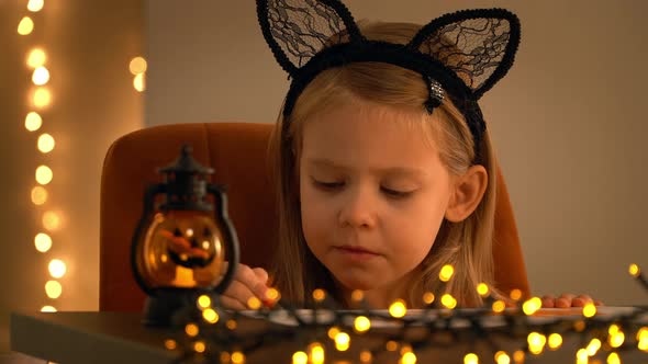 Child in Dark with Halloween Pumpkin Lamp Paints on Background of Garland Lights