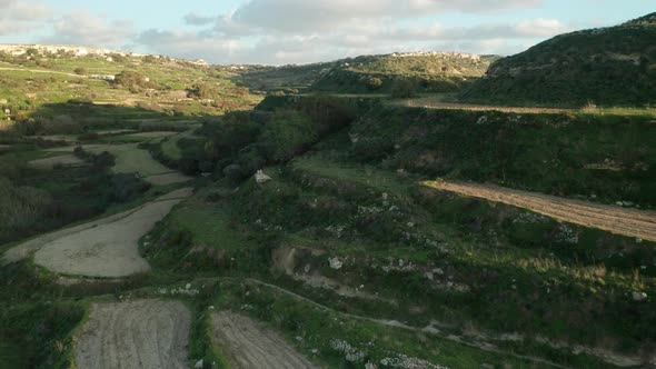 AERIAL: Flying Above Rocky Green Farmland on Hill on a Sunny Evening in Malta