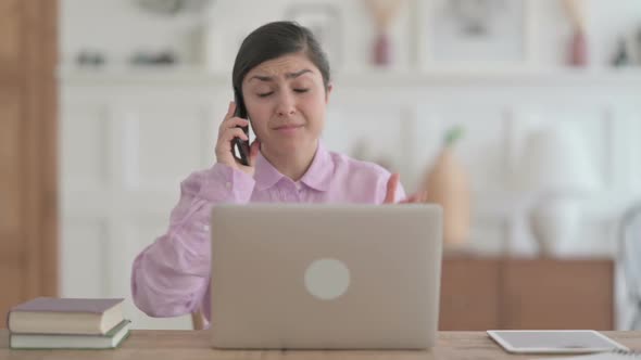 Angry Indian Woman Talking on Phone while using Laptop in Office alt