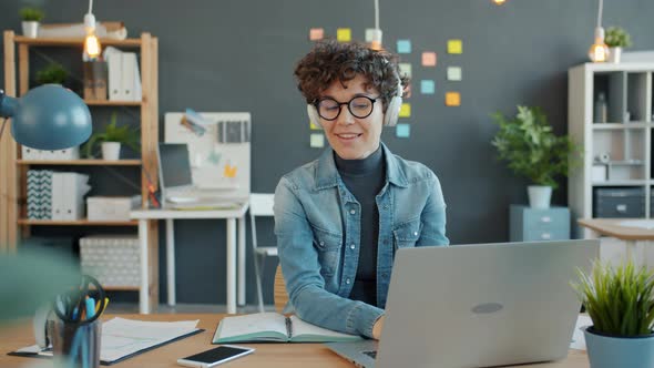 Cheerful Office Worker Using Laptop Computer Typing and Enjoying Music in Headphones alt
