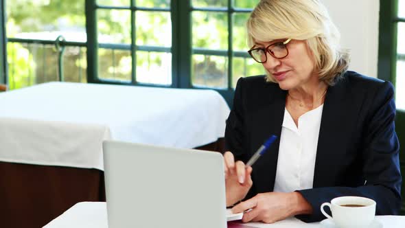 Businesswoman using laptop while having coffee alt