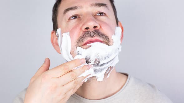 A Man Shaves His Beard and Mustache Closeup on a Gray Background