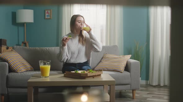 Girl in a white jacket is eating pizza and drinking orange juice