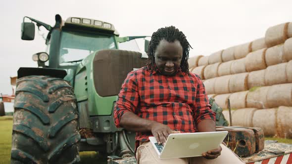 Thumb Up. Young African Farmer Using Tablet While Sitting on Green Tractor. Haystack in the alt