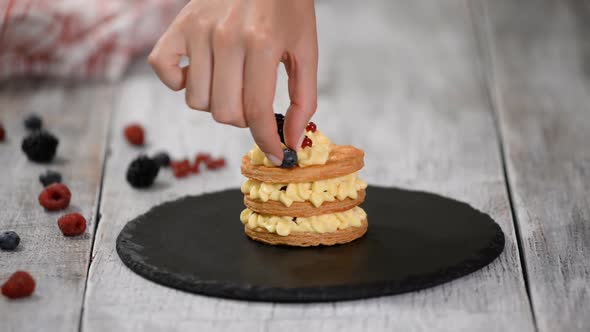 Pastry chef making French Mille Feuille with custard and berries.  alt