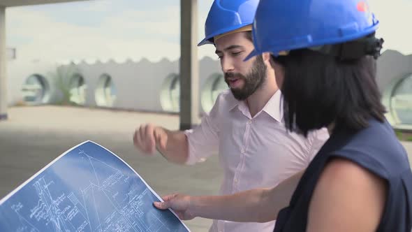 Man and woman discussing with blueprint at construction site