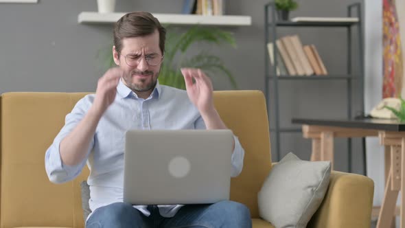 Young Man with Laptop Having Headache on Sofa alt