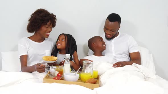 Happy family having breakfast together on bed alt