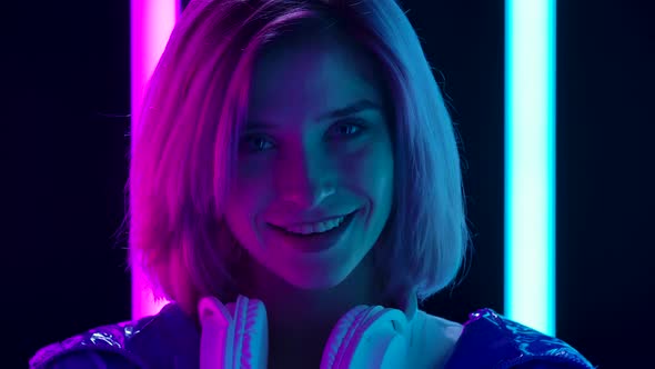 Portrait of a Young Stylish Woman with Big White Headphones Looking at the Camera and Smiling. Close alt