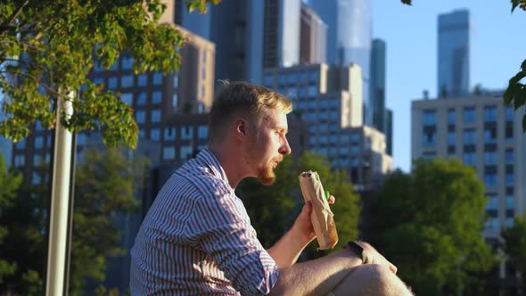 a man eats shawarma and drinks water in the background of skyscrapers